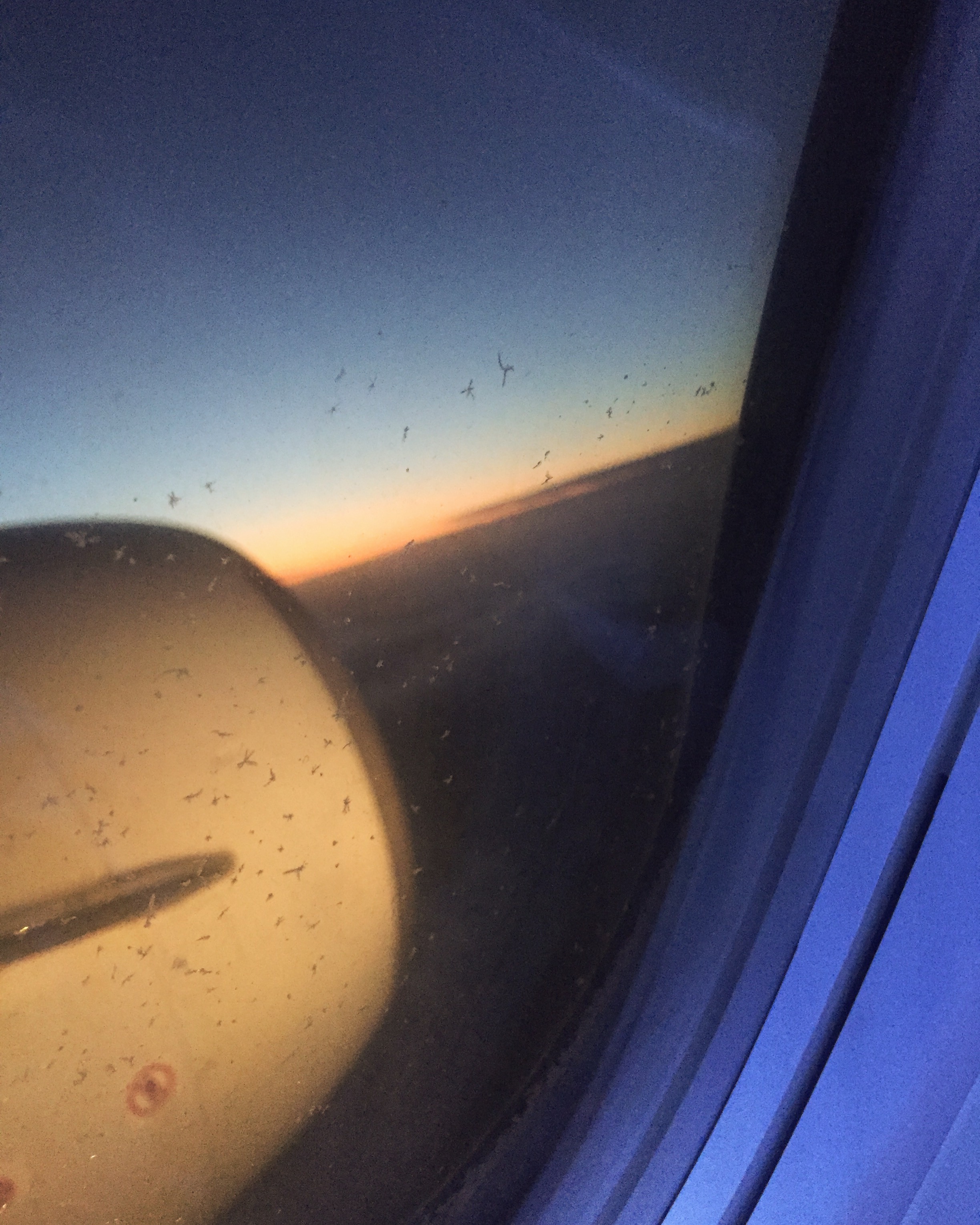 A photo taken through an aircraft window looking out across a sunset