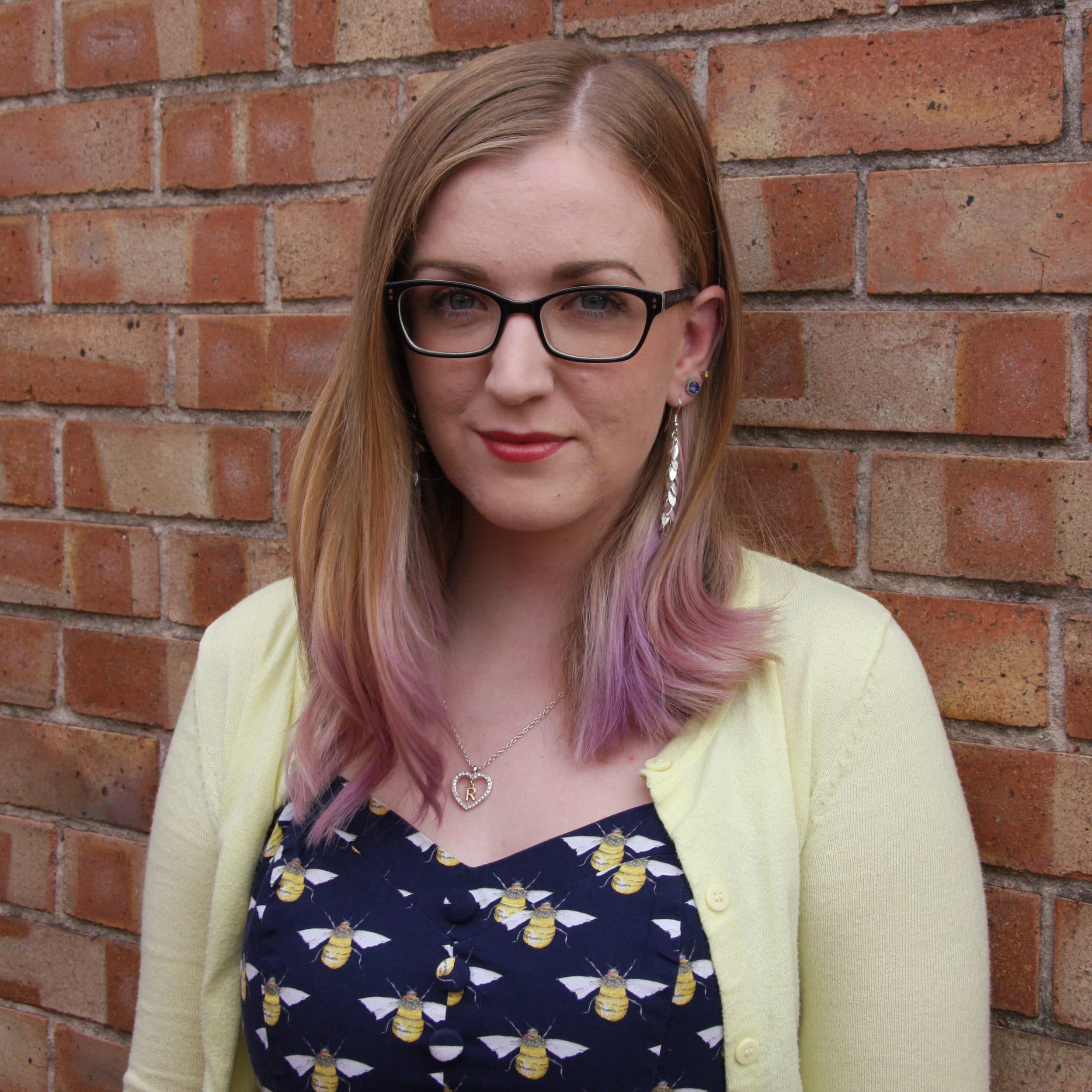 A headshot photo of Rachel stood in.front of a brick wall.