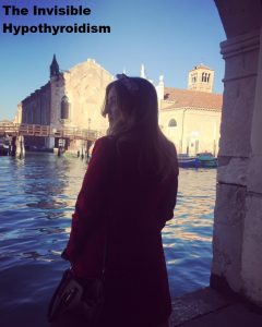A full length photo of Rachel facing away from the camera into the canals of Venice. In the background are boats and a wooden bridge lit up by the sun.