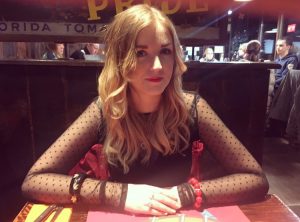 Rachel sitting in a restaurant, arms folded, looking into the camera. 